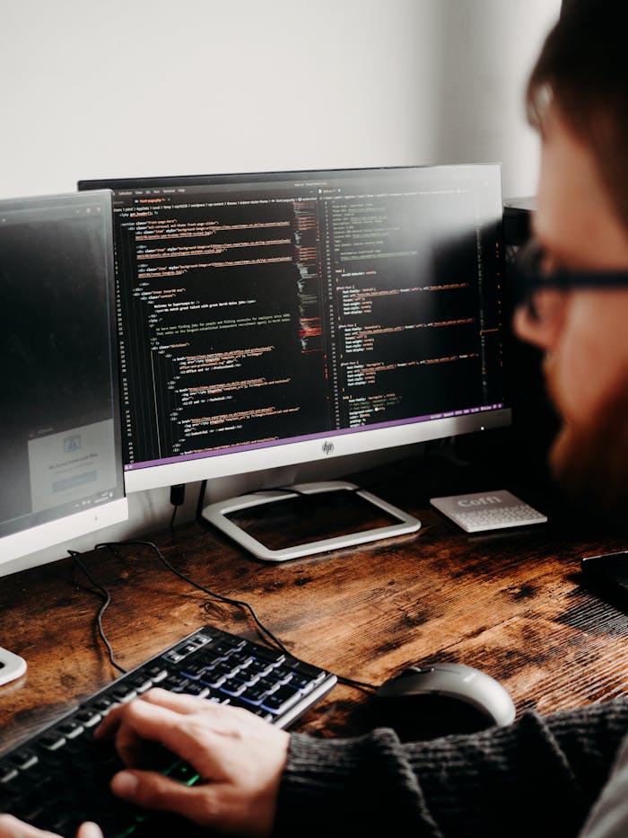 Focused software developer at desk coding with multiple monitors in a modern workspace.